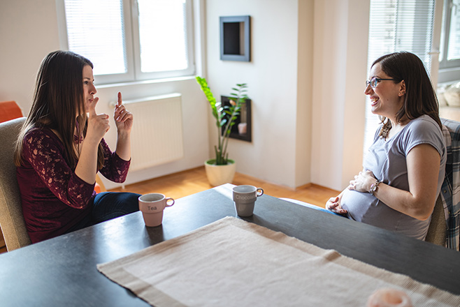Two ladies having a conversation at a dining table, one of which is doing sign language