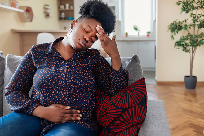 A woman on a couch holding her head and stomach
